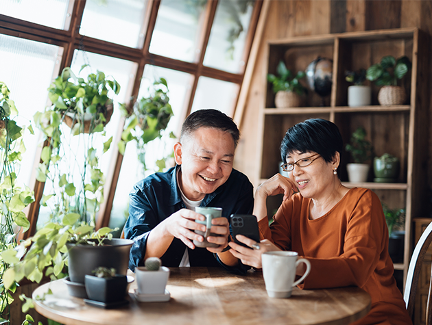 Elderly man and woman drinking from mugs and looking at phone.